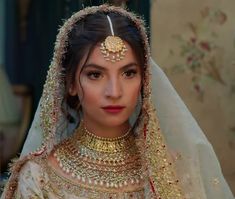 a woman wearing a bridal outfit with gold jewelry on her head and veil over her face