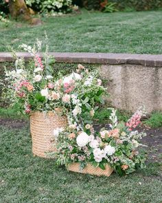 two baskets filled with flowers sitting on top of a grass covered field next to a stone wall