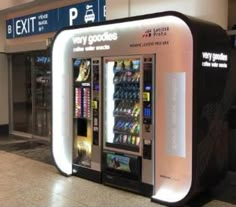 a vending machine in an airport lobby next to the exit sign that says very goodies