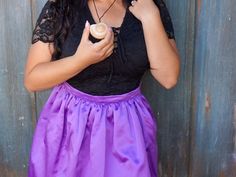 a woman wearing a black top and purple skirt holding a cupcake in her hand