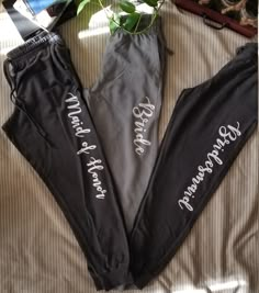 three black pants with white writing on them sitting on top of a bed next to a potted plant