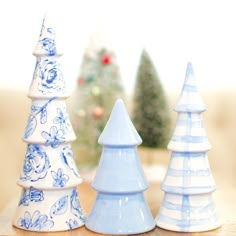 three blue and white ceramic christmas trees sitting on a table next to a small tree