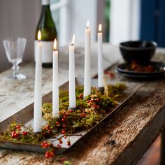 candles are arranged on a tray with moss and berries around it, along with wine glasses