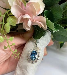 a person holding a bouquet of flowers with a blue stone in the center and surrounded by greenery