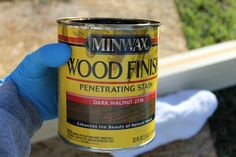 a person in blue gloves holding up a can of wood finishing stain next to a window