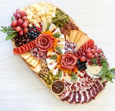 a platter filled with meats, cheeses and fruit on a white surface