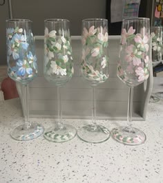 four wine glasses with flowers painted on them are lined up in a row and one is empty