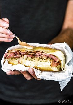 a person holding a hot dog with toppings and a spoon in their hand,