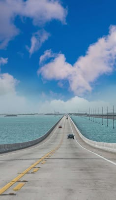 a car is driving down the road by the water and clouds in the blue sky