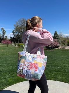 a woman carrying a multicolored patchwork tote bag on her back while walking in the park