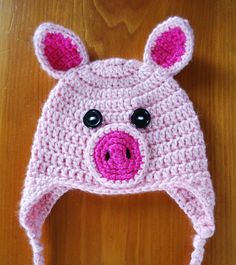 a crocheted pig hat with black eyes on a wooden table next to a pair of scissors