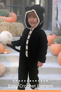 a young child in a black cat costume standing on steps with pumpkins and hay