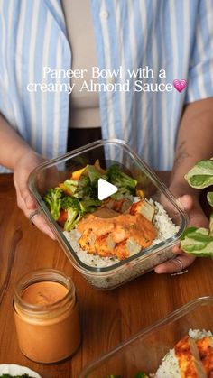 a person holding a bowl with food in it on top of a wooden table next to other dishes