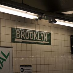 there is a sign that says brooklyn on the wall above tiles in a subway station