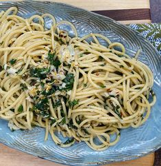 a blue plate filled with pasta and greens on top of a wooden table next to a fork