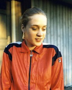 a woman wearing a red jacket and black pants standing in front of a garage door