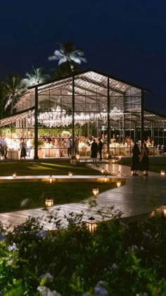 people are gathered outside at night in a glass pavilion with lit candles on the ground