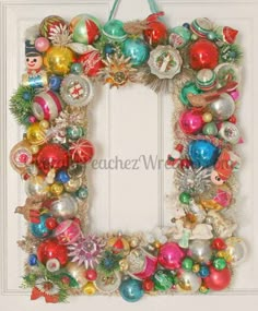 a christmas wreath with ornaments hanging on the front door and an empty frame in the middle