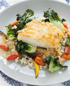 a white plate topped with fish and veggies on top of a blue and white table cloth