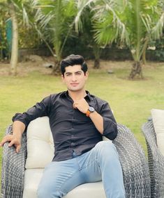 a man sitting on top of a white couch next to a lush green field with palm trees