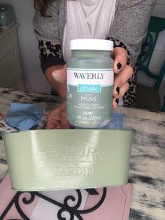 a woman holding a jar of wax on top of a table