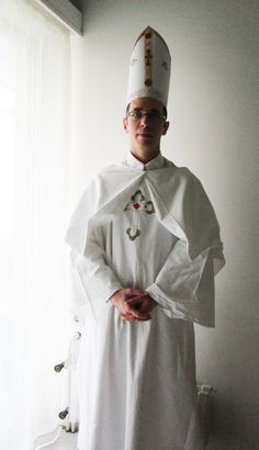 a man in a priest's outfit standing next to a window with his hands on his hips