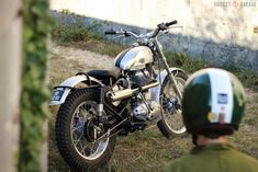 a motorcycle parked in the grass next to a man with a helmet on his head