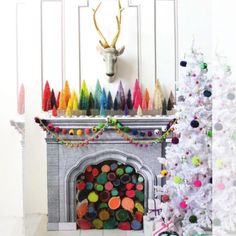 there is a christmas tree in front of the fireplace with colorful decorations on it and a deer head above