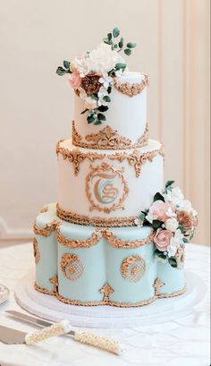 a three tiered cake decorated with flowers and gold trimmings on a table