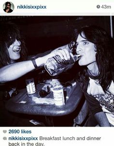 two women sitting at a table with drinks in their hands and one drinking from a bottle