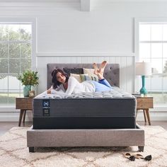 a woman laying on top of a bed in a room with white walls and windows