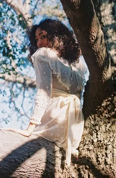 a woman in a white dress sitting on top of a tree