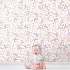 a baby sitting on the floor in front of a wallpapered with pink and purple flowers