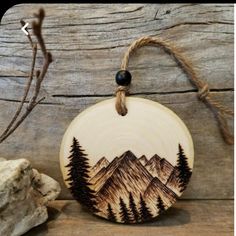 a wooden ornament with mountains and trees on it, hanging from a rope