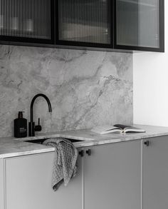 a kitchen with marble counter tops and black cabinetry, along with a book open to the side