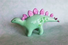 a green toy dinosaur with pink spikes on it's head and tail, sitting on a patterned surface