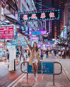 a woman standing on a rail in the middle of a city at night with neon signs above her