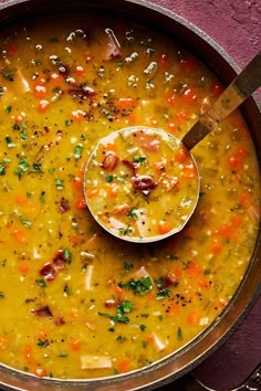 a large pot filled with soup on top of a purple table cloth next to a wooden spoon