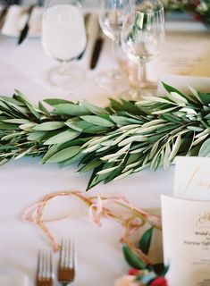 the table is decorated with greenery and place settings for guests to sit down at