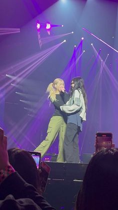 two women on stage hugging each other with their arms around one another as the crowd looks on