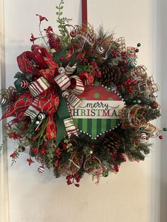 a wreath hanging on the front door with merry christmas written in green, red and white