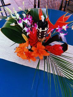 an arrangement of flowers on a blue table cloth with palm leaves and vases in the background