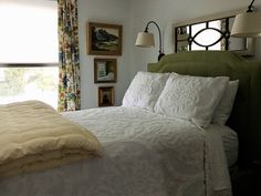 a bed with white comforter and pillows in a bedroom next to a large window