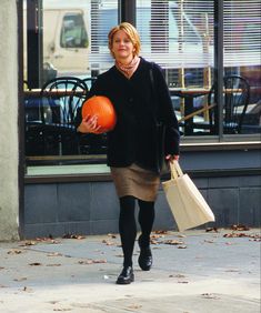 a woman is walking down the street carrying bags and an orange ball in her hand