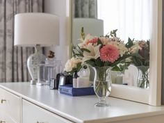 a vase filled with flowers sitting on top of a white dresser next to a mirror