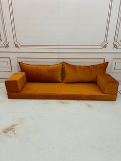 an orange couch with two pillows on it in front of a white wall and ceiling