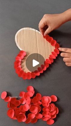 someone is making a heart out of paper and some red circles on the table with their hands