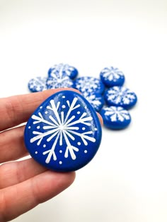 a hand holding a blue and white painted rock with snowflake designs on it