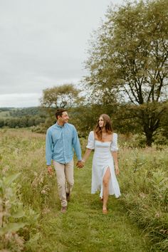 a man and woman holding hands while walking through tall grass in the middle of a field