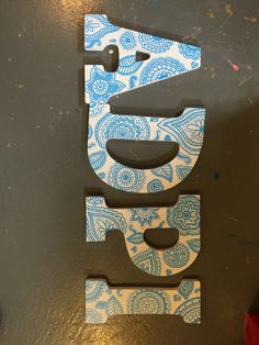 the letter e is made out of wood and has blue paisley designs on it's sides